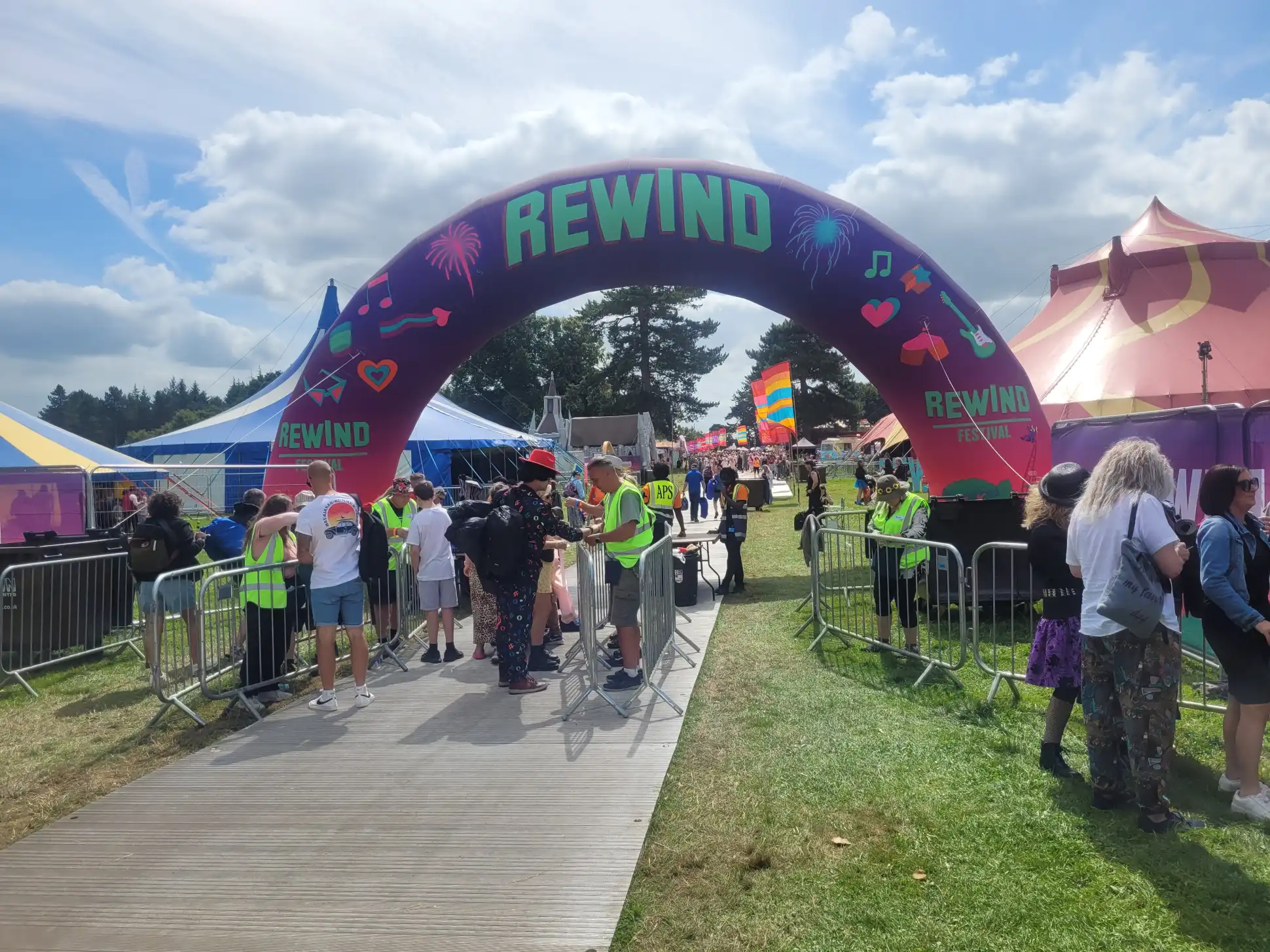 The entrance arch to Rewind Festival North 2024 with staff checking tickets and the festival site visible in the background