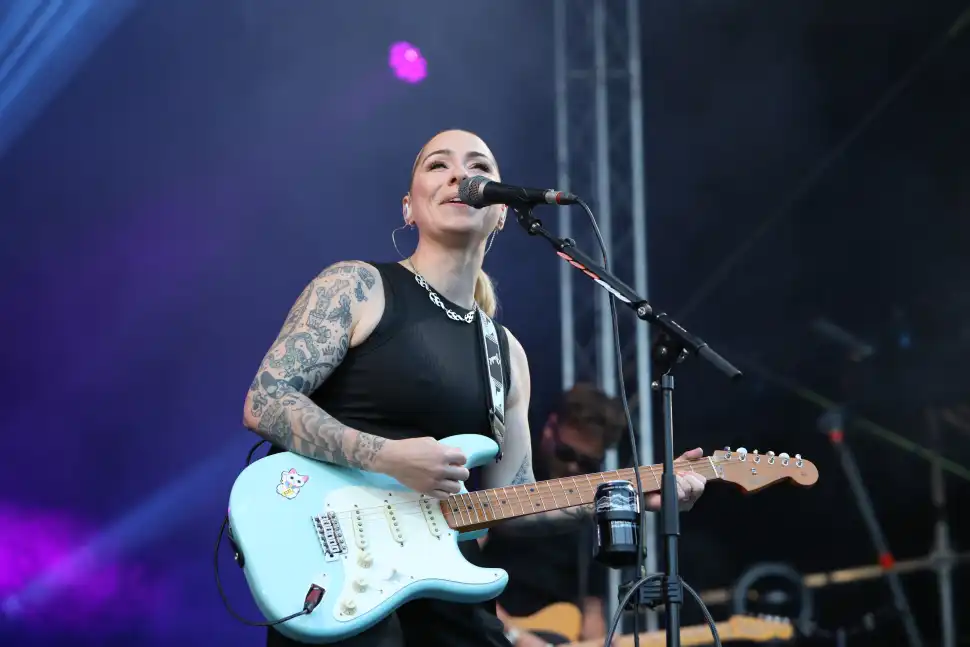 Lucy Spraggan beams while singing to crowd whilst playing a sky-blue electric guitar