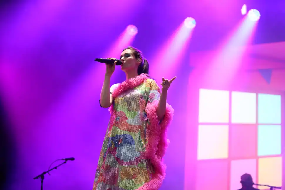 Sophie Ellis Bextor singing on stage in a colourful dress against a purple background