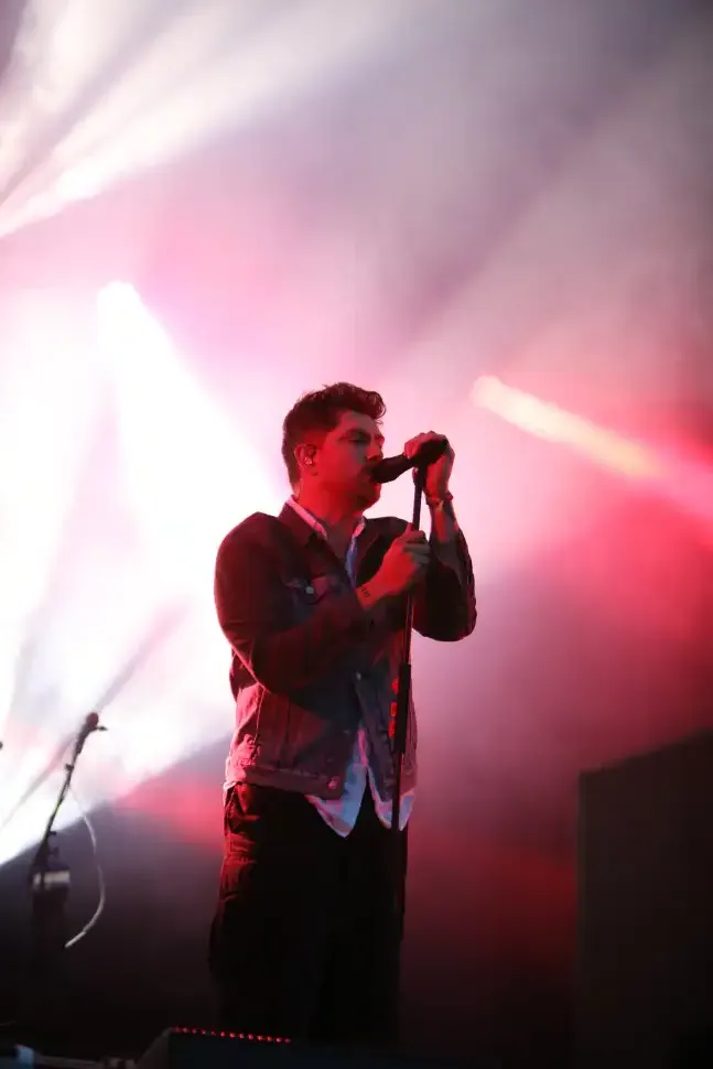 Sam McTrusty of Twin Atlantic sings softly into the mic with bright colourful stage lighting behind him