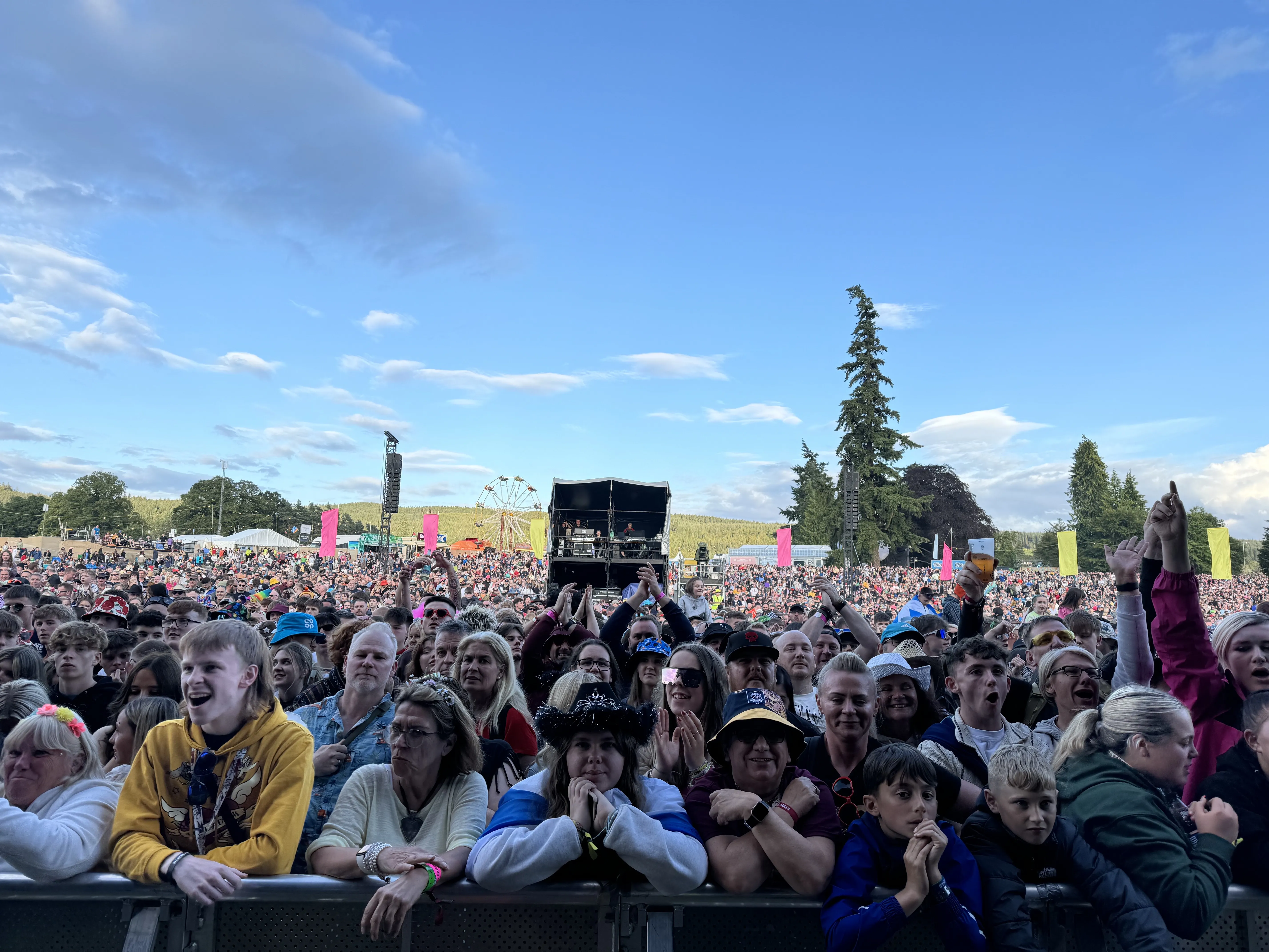 Festival crowd looking at the stage in the photographer's direction with a ferris wheel and blue skies behind them